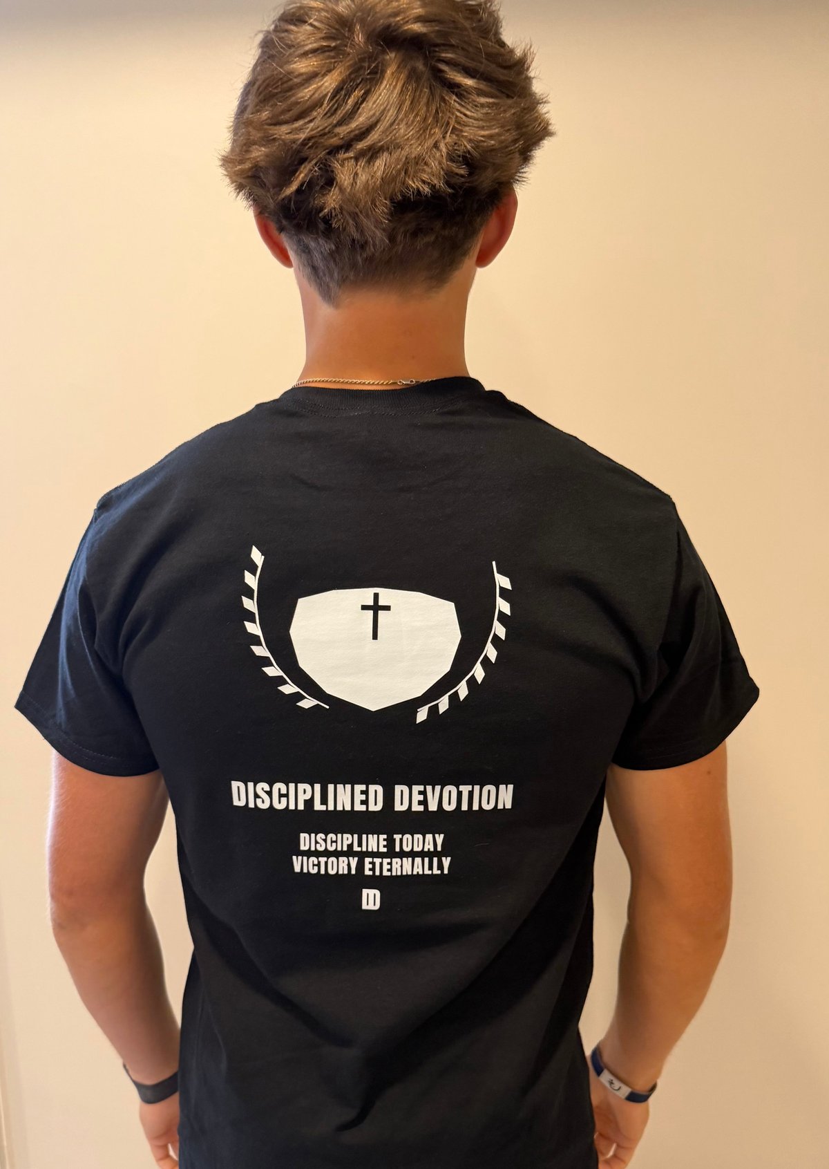 Person wearing black t-shirt with Disciplined Devotion graphic design featuring a cross and text on the back